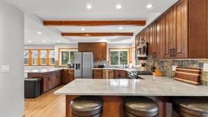 A modern kitchen with wooden cabinets, a large island with stools, stainless steel appliances, and a stone backsplash. - Bottle Bay View Lodge – 21-Acre Lakefront Retreat (Sagle)