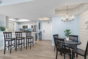 A modern kitchen with white cabinets, a central island, and a dining area with dark wooden chairs and a round table. - St. Lucia 1202 (Destin)