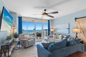 A spacious living room with a large window offering a view of the ocean, a ceiling fan, and a cozy seating area with a blue sofa and armchairs. - St. Lucia 1202 (Destin)