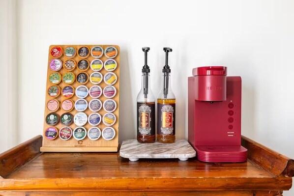 A coffee machine, two bottles of coffee, and a board with coffee pods on a wooden tray.