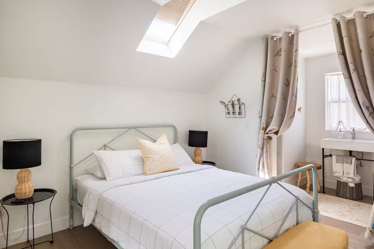 A modern bedroom with a bed, two bedside tables, a desk, and a window with curtains.
