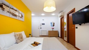 A hotel room with a bed, a TV, a mirror, and a door. - Studio Apartment --1 (Yerevan)
