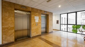 A modern elevator area with two elevators, a marble wall, and a large window with a view of buildings. - Studio Apartment --1 (Yerevan)