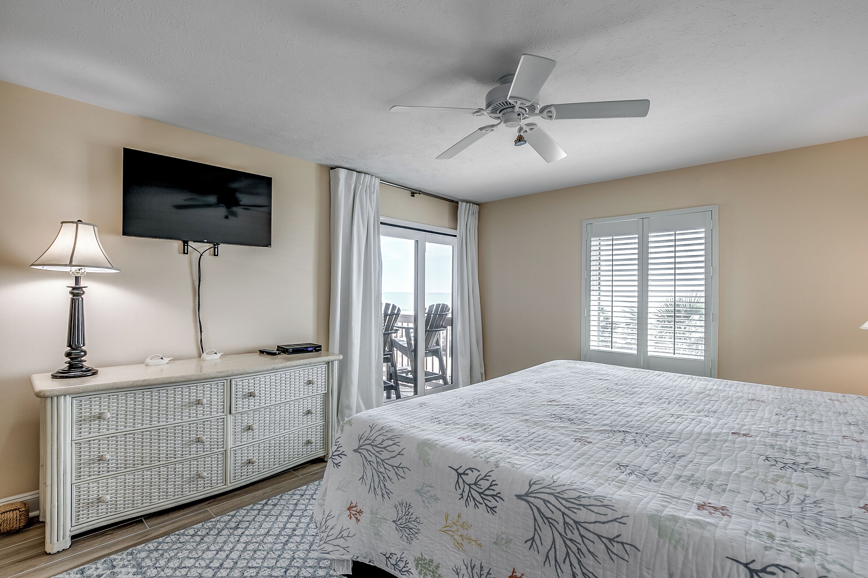 A bedroom with a bed, a ceiling fan, a TV, a dresser, and a window with blinds.