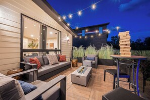 An outdoor patio area with a sofa, a coffee table, and a seating arrangement. - Riverside Hot Tub, Cedar Sauna & Arcade Games (Hunter)