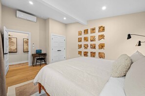 A bedroom with a large bed, a desk with a chair, and a door leading to another room. - Riverside Hot Tub, Cedar Sauna & Arcade Games (Hunter)