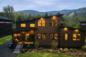Une maison moderne à deux étages, dotée d’un porche à l’avant, de grandes fenêtres et offrant une vue sur les collines environnantes.