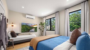 Une chambre moderne avec un grand lit, un canapé, une fenêtre donnant sur des arbres et un appareil de climatisation.