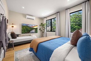 A modern bedroom with a large bed, a sofa, a window with a view of trees, and an air conditioning unit. - Riverside Hot Tub, Cedar Sauna & Arcade Games (Hunter)