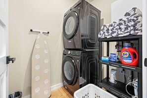 Un espace buanderie comprenant deux machines à laver superposées, un étendoir et une étagère avec des produits de nettoyage.