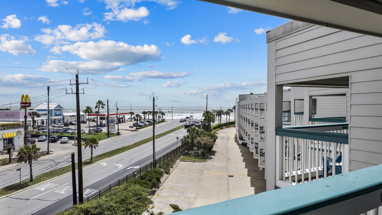 A coastal road with commercial establishments, a clear sky, and a building with balconies.