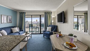 Une chambre d’hôtel avec balcon, une table à manger où le petit-déjeuner est servi, un canapé et un téléviseur.