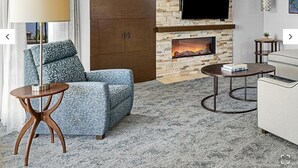 Un salon moderne doté d’une cheminée en pierre, d’un téléviseur à écran plat et d’un coin salon confortable avec un canapé à motifs et une table basse ronde.