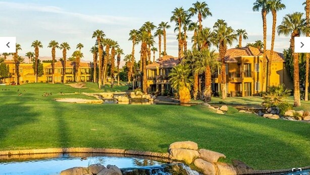 Un parcours de golf agrémenté d’un plan d’eau, de palmiers et d’un grand bâtiment doté de nombreux balcons.
