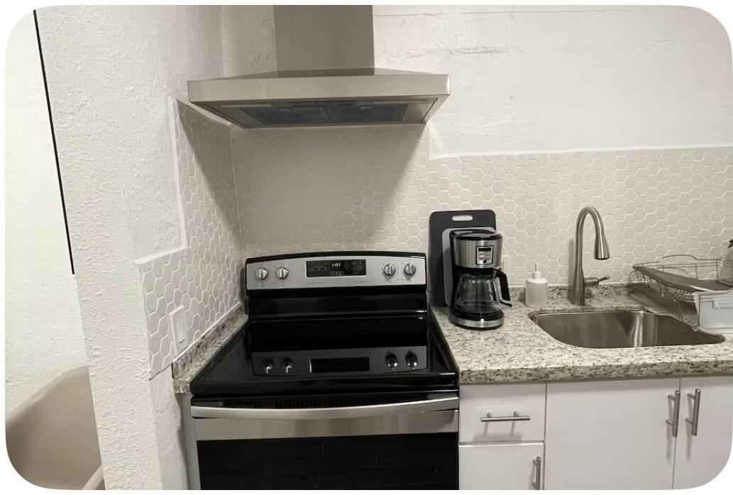 Een kleine keuken met een fornuis, koffiezetapparaat en wasbak.