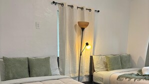 Une chambre avec deux lits, une lampe sur pied et une fenêtre avec des rideaux.