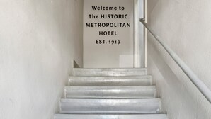 Een trap die leidt naar een kamer, met een bord waarop staat: Welkom bij HET HISTORISCH METROPOLITAN HOTEL OPRICHTING 1919.