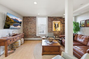 A living room with a brick wall, a mounted TV, a leather couch, a wooden coffee table, and a painting of a bull.