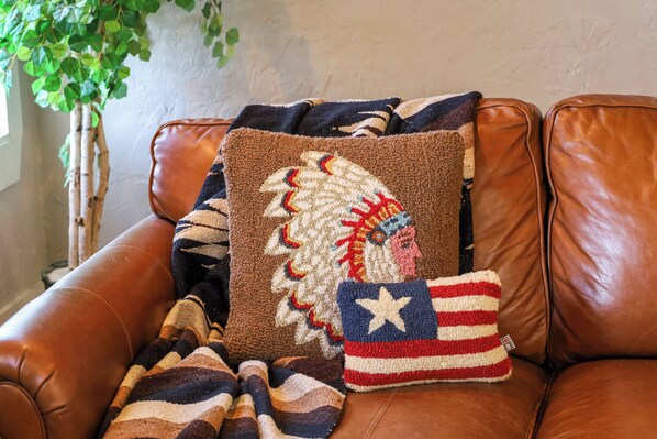 Un sofá de cuero marrón con un cojín de tocado nativo americano y un cojín pequeño con diseño de estrellas y rayas.