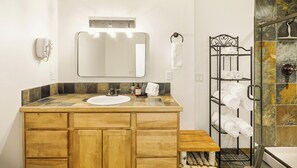 A bathroom with a wooden vanity, a large mirror, a towel rack, and a shower area with a tiled wall.
