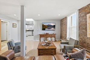 Una sala de estar moderna con chimenea, sofás de cuero, una mesa de centro de madera y un ventanal con persianas.