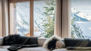 Una habitación acogedora con un amplio ventanal que ofrece vistas a montañas nevadas y una cabaña.