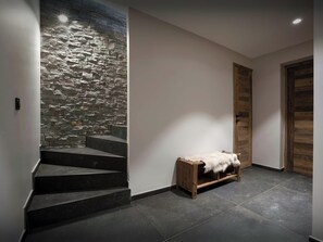 A staircase with a stone wall, a wooden bench with a fur throw, and a wooden door. - Chalet Fango - Splendid modern chalet with sauna and hot tub - OVO Network (Les Belleville)