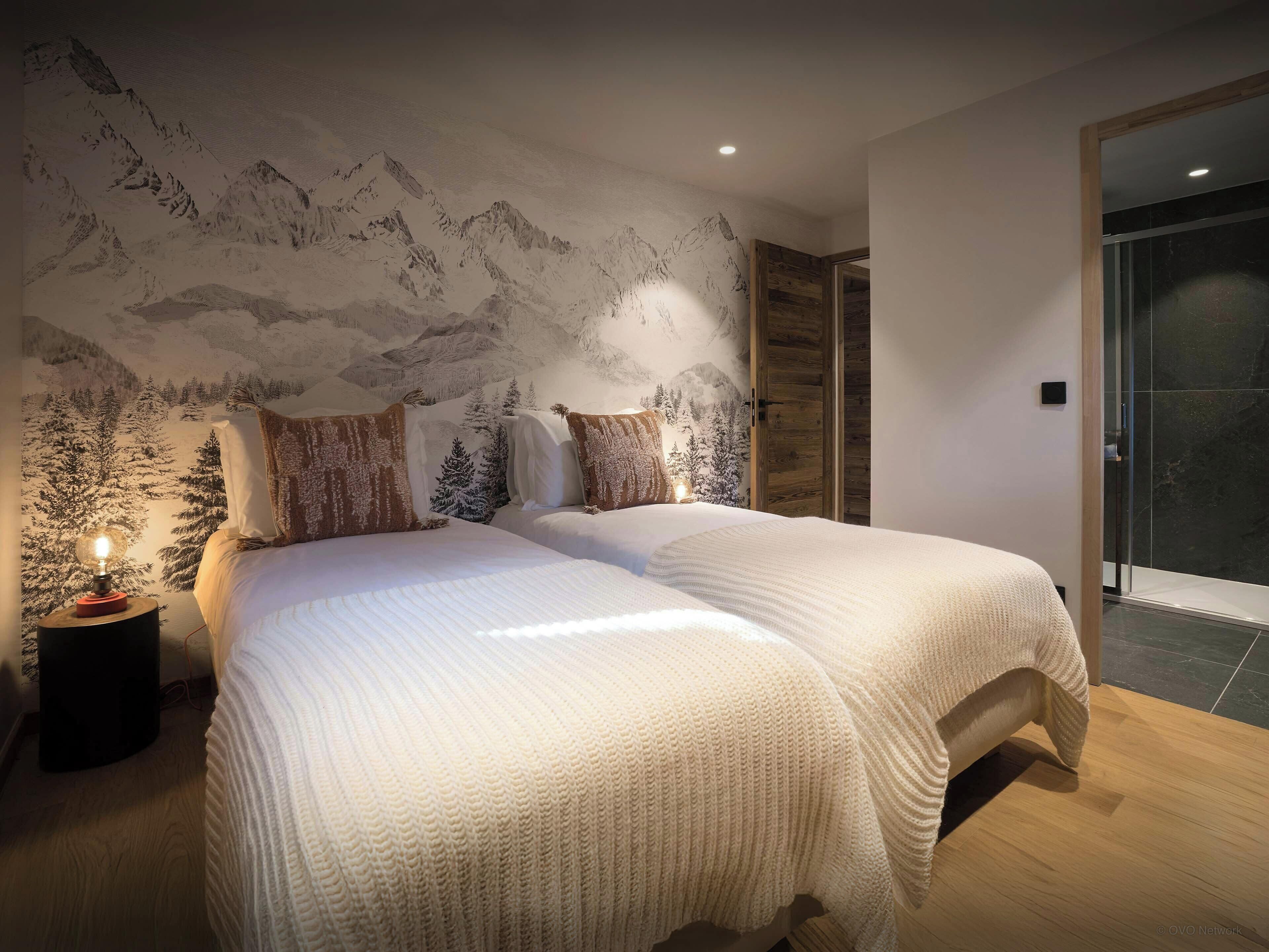A bedroom with a large bed, a nightstand, and a wall mural of a mountainous landscape.