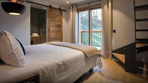 A modern bedroom with a large bed, a wooden wardrobe, a balcony with a railing, and a staircase. - Chalet Fango - Splendid modern chalet with sauna and hot tub - OVO Network (Les Belleville)