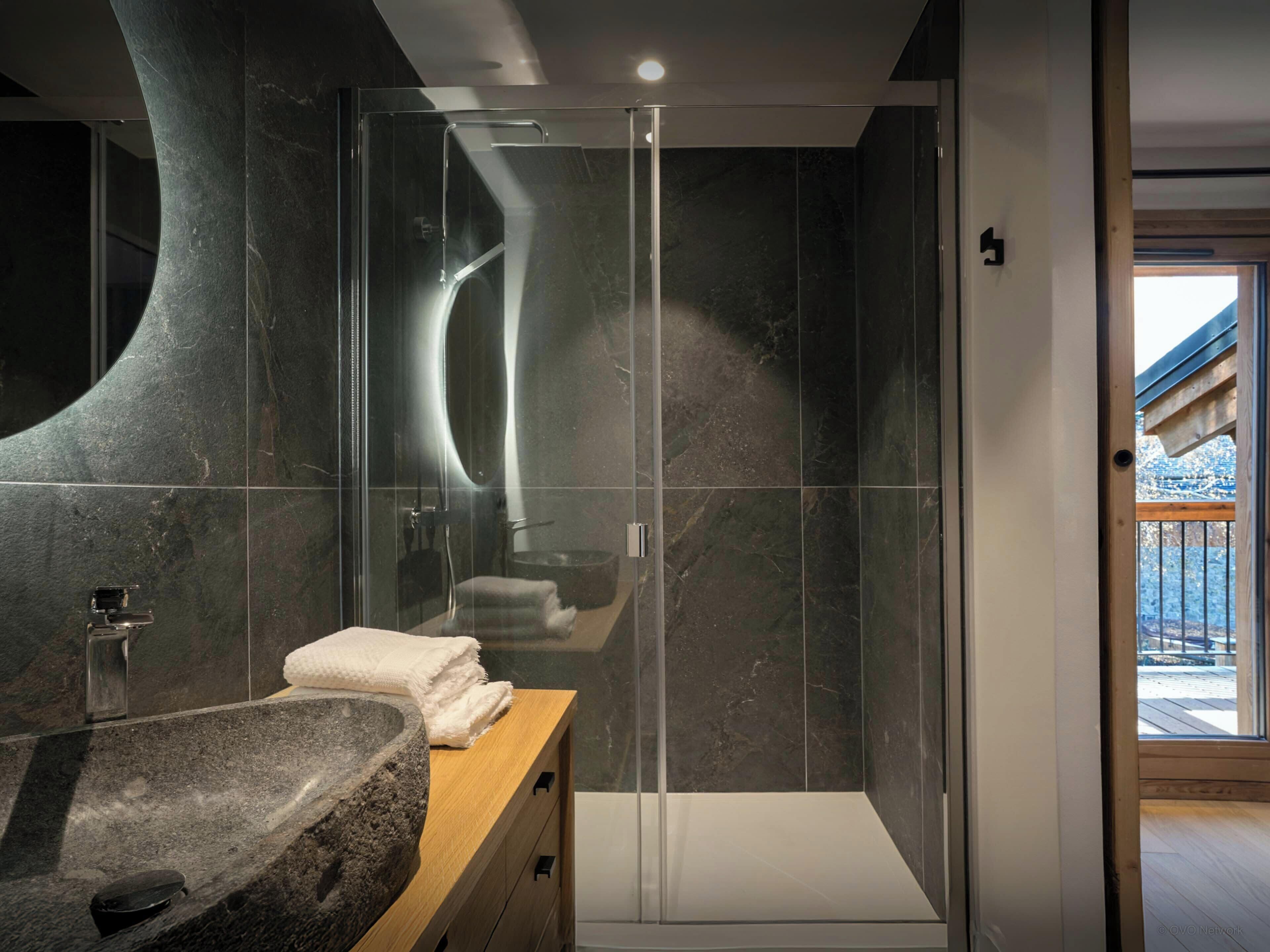 A modern bathroom with a stone sink, a glass shower enclosure, and a wooden vanity.