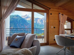 A cozy room with a sofa and armchair, large windows offering a mountain view, and a balcony with a railing. - COCO CHATEL - Discover the traditional charm of Châtel for 6 - OVO Network (Châtel)