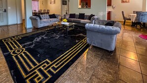A spacious living room with a black and gold patterned rug, grey sofas, and a dining area in the background. - Luxury Vacation Rental (Las Cruces)