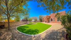 A well-maintained backyard with a green lawn, a stone wall, and a modern building with large windows. - Luxury Vacation Rental (Las Cruces)