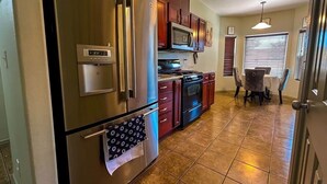 A kitchen with stainless steel appliances, a microwave, and a stove. There is a dining table with chairs and a window with blinds. - Luxury Vacation Rental (Las Cruces)