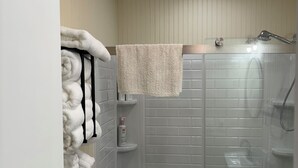 A modern bathroom with a glass shower enclosure, a towel rack with folded towels, and a small shelf with toiletries.