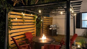 A covered outdoor patio with a fire pit, red chairs, and a grill.