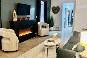 A modern living room with a fireplace, a television, and a heart-shaped wall decoration. - The Cozy Mitten – , 2 Bedroom/1 Bath, Fenced Yard & Laundry (Muskegon)