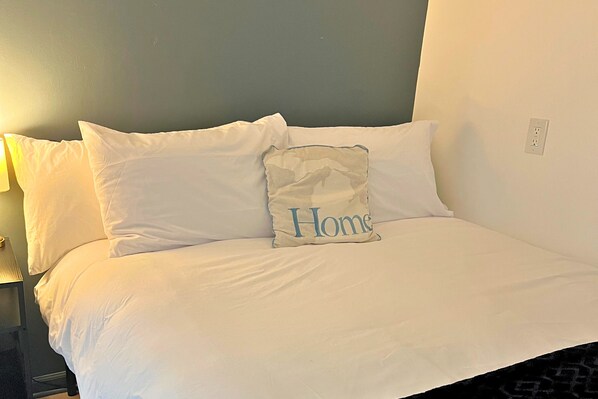A neatly made bed with white bedding and a pillow with "Home" written on it. - The Cozy Mitten – , 2 Bedroom/1 Bath, Fenced Yard & Laundry (Muskegon)