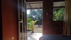 A bedroom with a bed, a sliding glass door leading to an outdoor area with a potted plant, and a window with curtains.