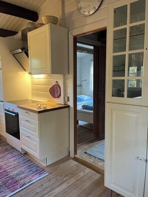 A compact kitchen with white cabinets, a stove, and a red heart-shaped decoration. - Log cabin on Fanø near beach and nature (Fanø)
