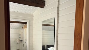 A narrow hallway with a bed, bedside table, lamp, and a mirror on the wall. - Log cabin on Fanø near beach and nature (Fanø)