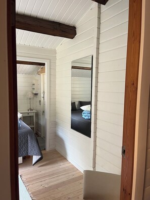 Ein schmaler Flur mit einem Bett, einem Nachttisch, einer Lampe und einem Spiegel an der Wand.