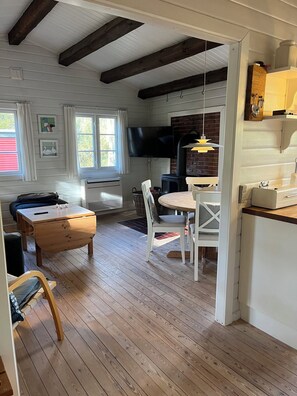 A cozy room with a wooden floor, a dining table with chairs, a TV mounted on the wall, and a fireplace. - Log cabin on Fanø near beach and nature (Fanø)