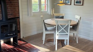A cozy room with a fireplace, a dining table with chairs, and a window with curtains. - Log cabin on Fanø near beach and nature (Fanø)