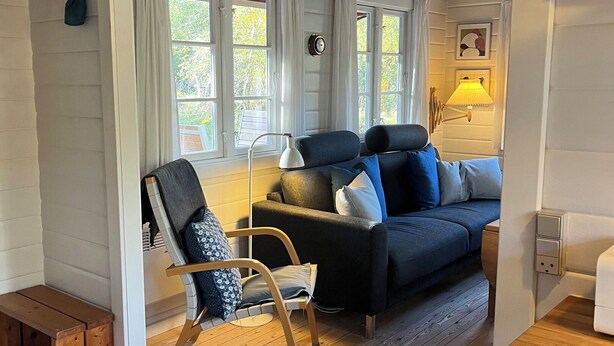 A cozy living room with a wooden floor, a sofa, a chair, and a lamp. - Log cabin on Fanø near beach and nature (Fanø)