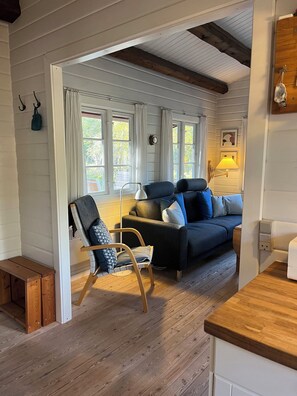 A cozy living room with a wooden floor, a sofa, a chair, and a lamp. - Log cabin on Fanø near beach and nature (Fanø)