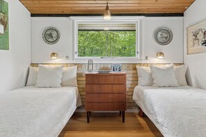 Ein Schlafzimmer mit zwei Betten, einer Holzkommode, einem Fenster mit Blick auf Bäume und Wandlampen.
