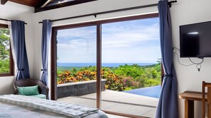Ein Zimmer mit einer großen Schiebetür, die auf einen Balkon mit Blick auf das Meer und üppige Vegetation führt.