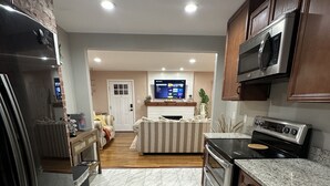 A modern kitchen with a built-in oven, microwave, and refrigerator. There is a dining area with a striped couch and a flat-screen TV. - ★ Superhost Rated ★ Lily of the Valley Retreat - Steps to Downtown (Kingsport)