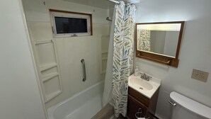 A bathroom with a shower, a window, a sink, and a toilet.